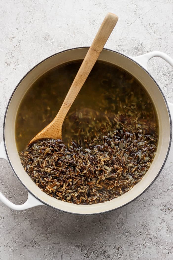 Wooden spoon stirring wild rice in pot of broth.