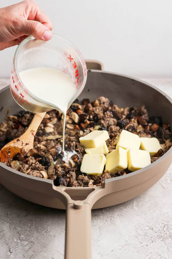 Pouring cream into wild rice casserole with cubes of butter.