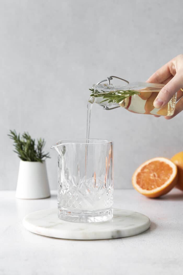 A hand pouring rosemary simple syrup into a cocktail glass