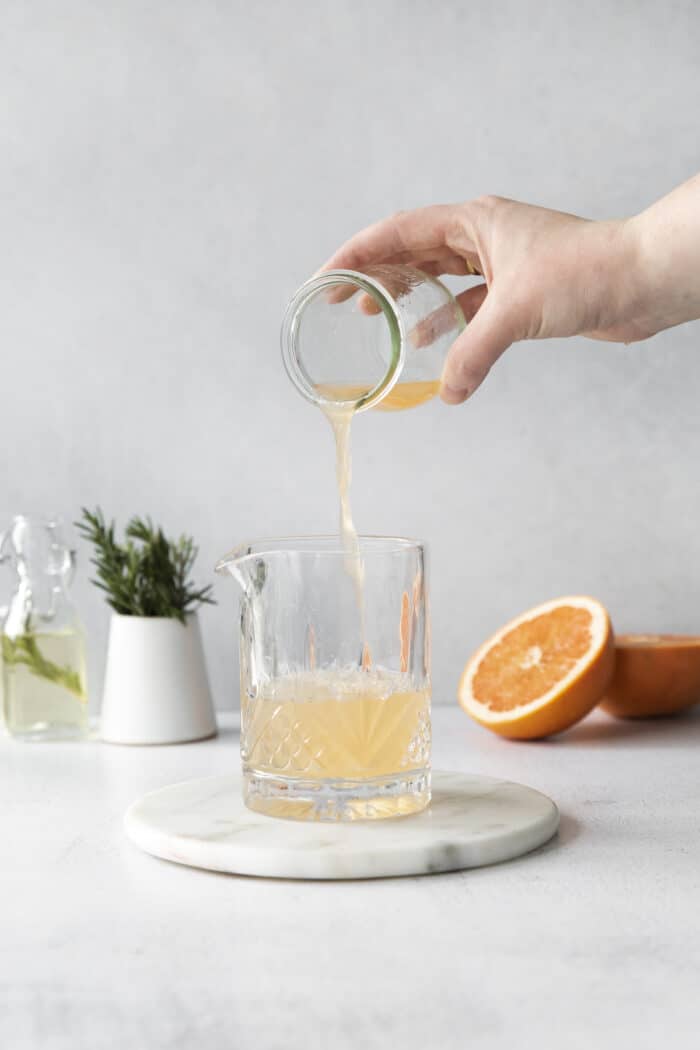 A hand pouring grapefruit juice into a cocktial glass