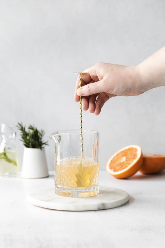 A spoon stirring ingredients in a cocktail glass