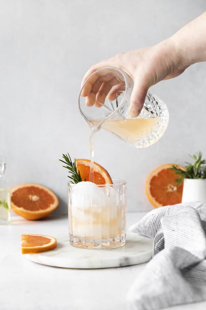 Grapefruit juice being poured over ice in a cocktail glass