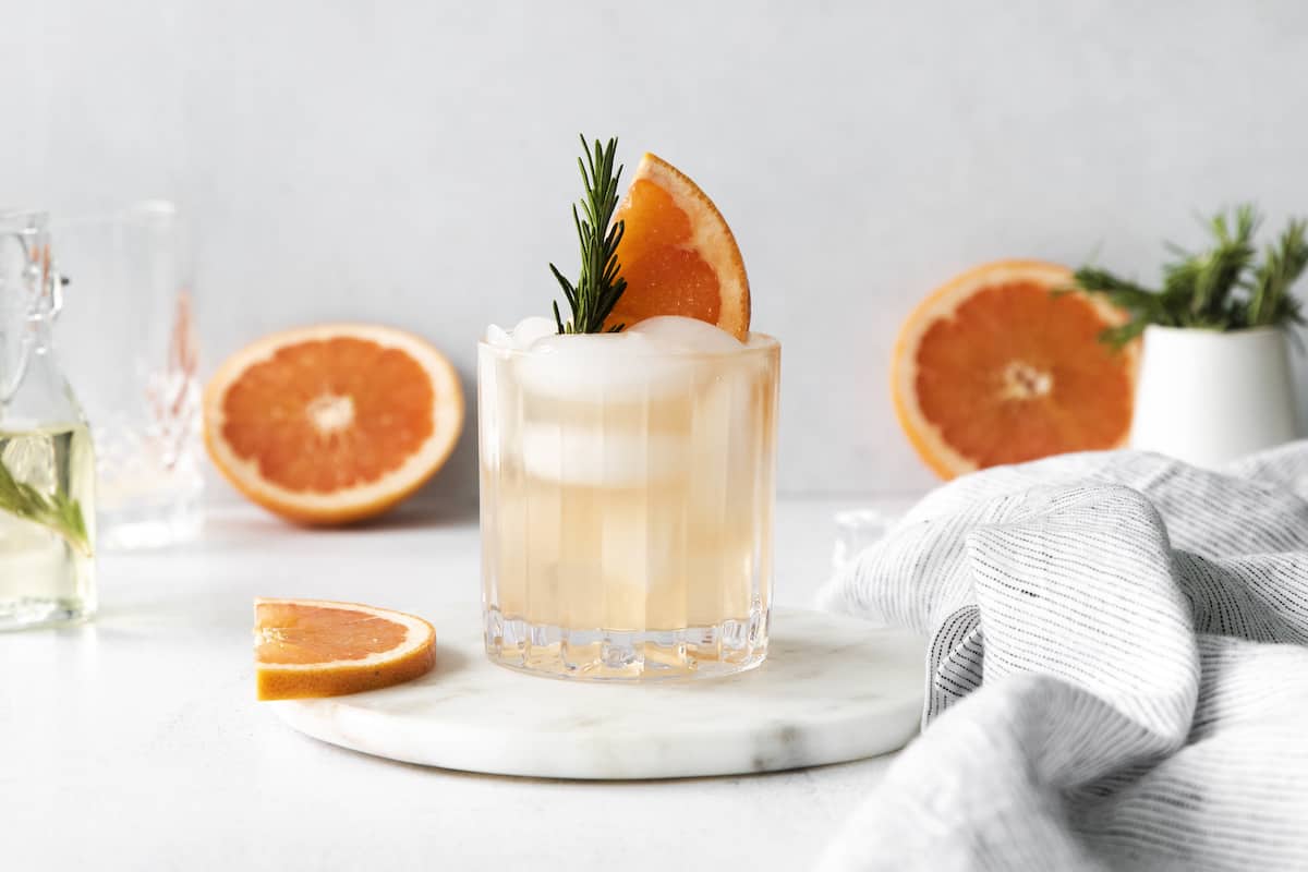 A rosemary greyhound cocktail with grapefruit halves in the packground