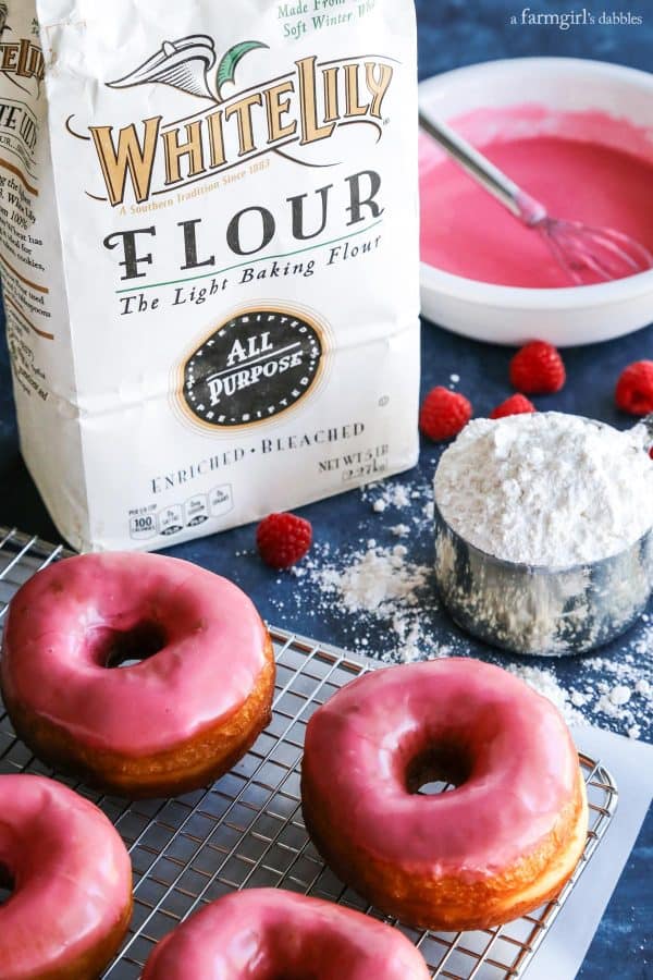 Yeast Donuts with Raspberry Glaze surrounded by a bag of flour and a measuring cup
