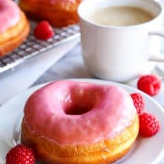 Homemade raspberry donuts with a cup of coffee in the background.