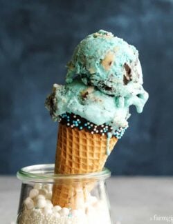 Cookie Monster Ice Cream in a dipped cone propped up inside a glass filled with white sprinkles.