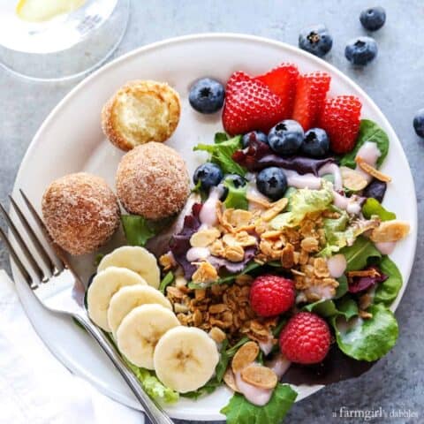 breakfast salad on a white plate topped with granola, served with berries and bananas