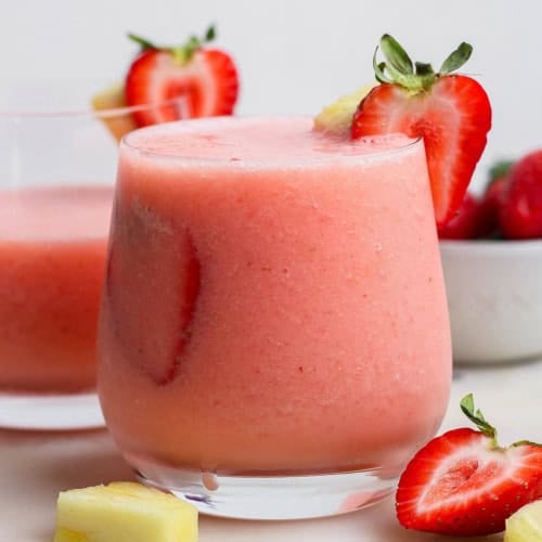 Frozen strawberry piña colada in glass with fresh strawberries for garnish.
