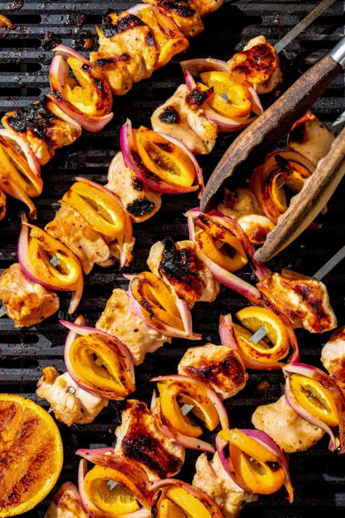 Overhead view of grilled chipotle orange turkey kabobs on grill, being turned with tongs