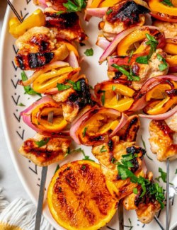 Overhead view of grilled chipotle orange turkey kabobs on platter with grilled orange half
