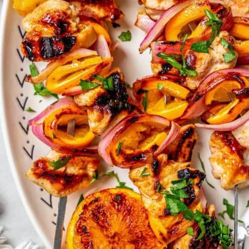 Overhead view of grilled chipotle orange turkey kabobs on platter with grilled orange half