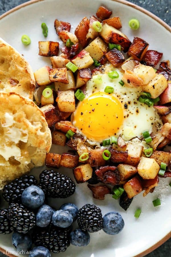 potato hash on a plate with English muffin and fresh blueberries and blackberries