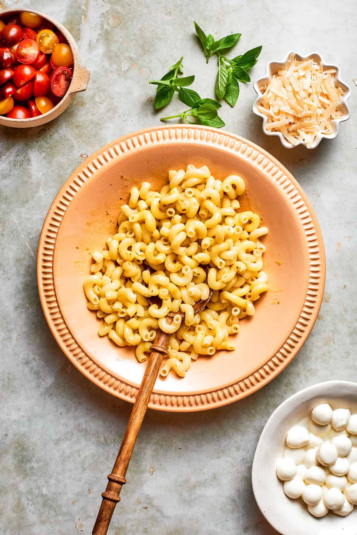 Cavatappi is tossed with juicy tomatoes, creamy mozzarella, basil, Parmesan and a bright balsamic dressing in this fresh caprese pasta salad. Pasta added to bowl with vinaigrette.