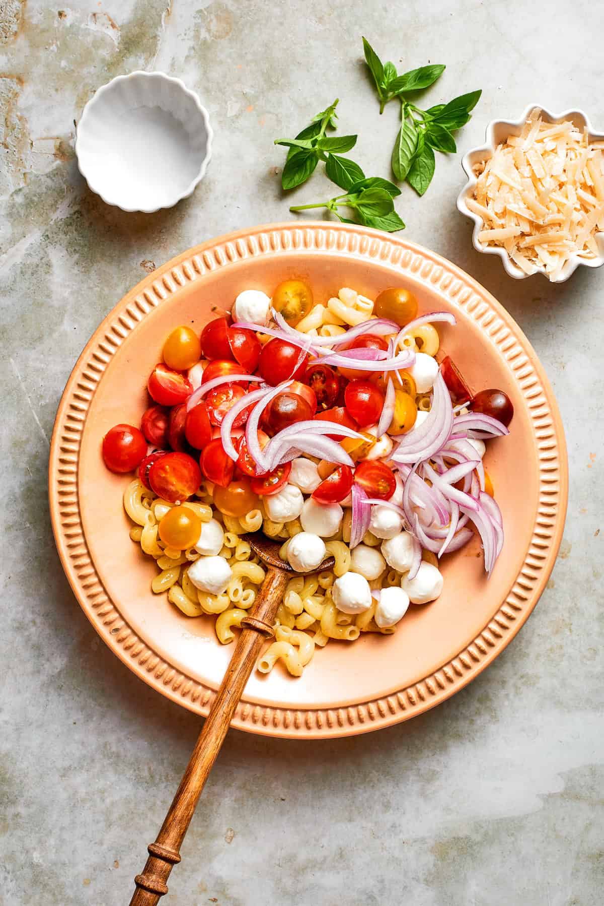 Cavatappi is tossed with juicy tomatoes, creamy mozzarella, basil, Parmesan and a bright balsamic dressing in this fresh caprese pasta salad. Onions, tomatoes, and mozzarella added to bowl of pasta.