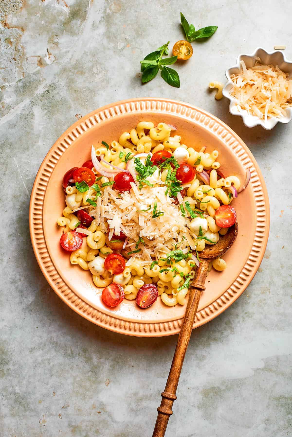 Cavatappi is tossed with juicy tomatoes, creamy mozzarella, basil, Parmesan and a bright balsamic dressing in this fresh caprese pasta salad. Spoon in bowl with caprese pasta salad.