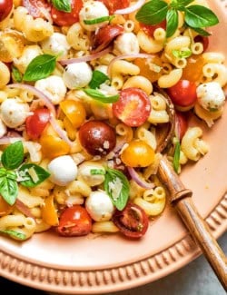 Caprese pasta salad in bowl with wooden spoon.
