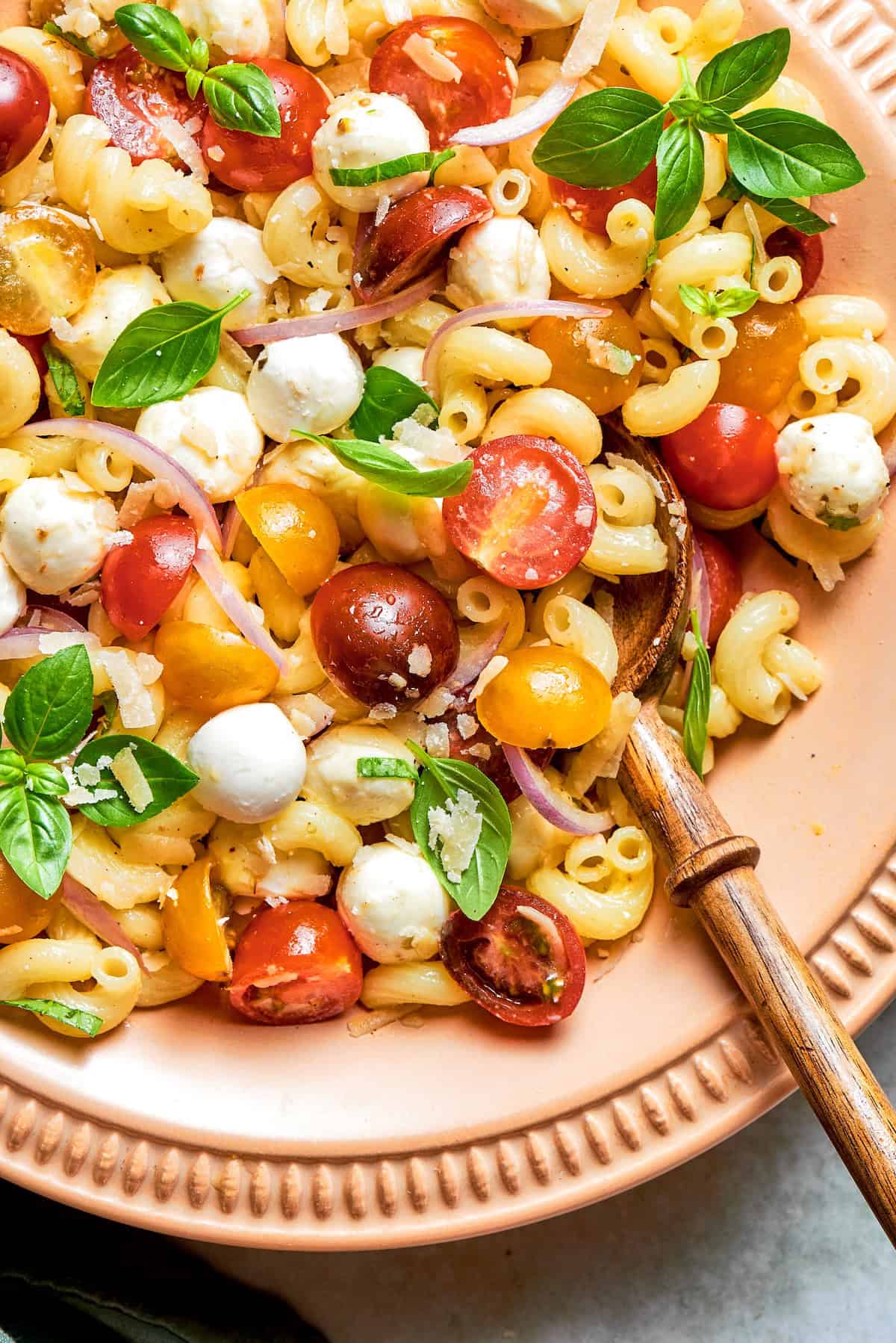 Cavatappi is tossed with juicy tomatoes, creamy mozzarella, basil, Parmesan and a bright balsamic dressing in this fresh caprese pasta salad. Caprese pasta salad in bowl with wooden spoon.