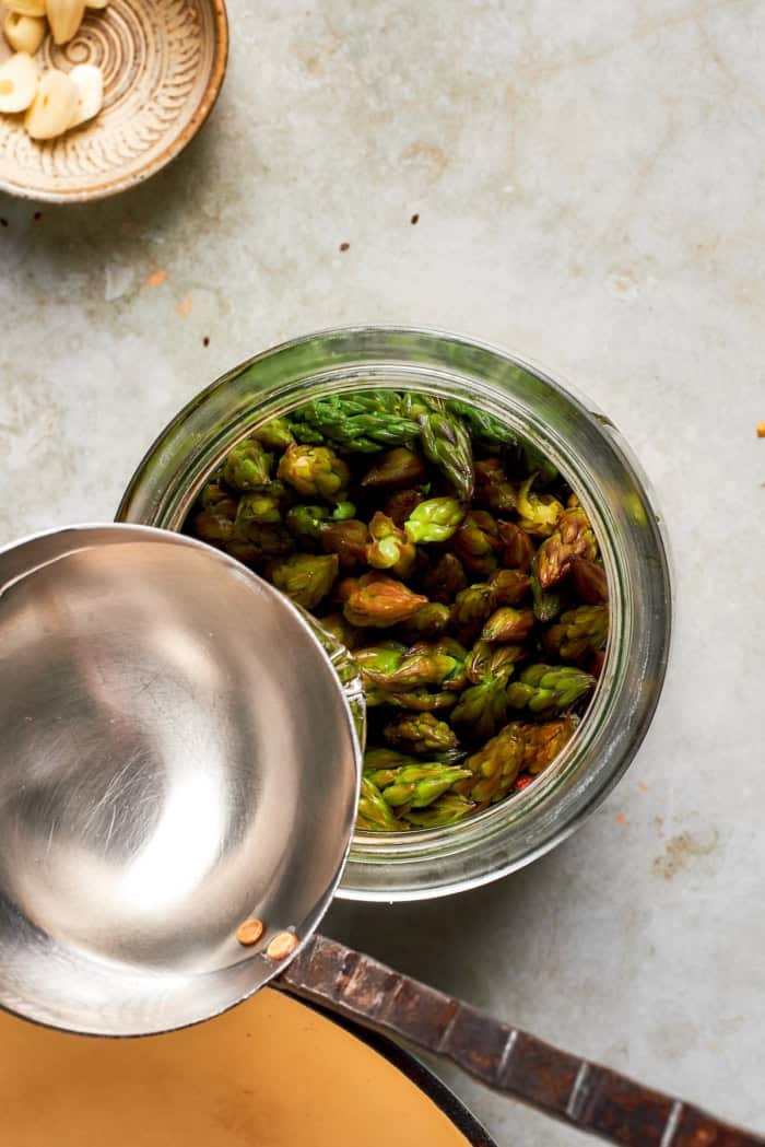Pouring brine into jar of asparagus.