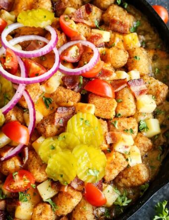 Tater tots with sliced pickles, tomatoes and red onion in a cast iron skillet