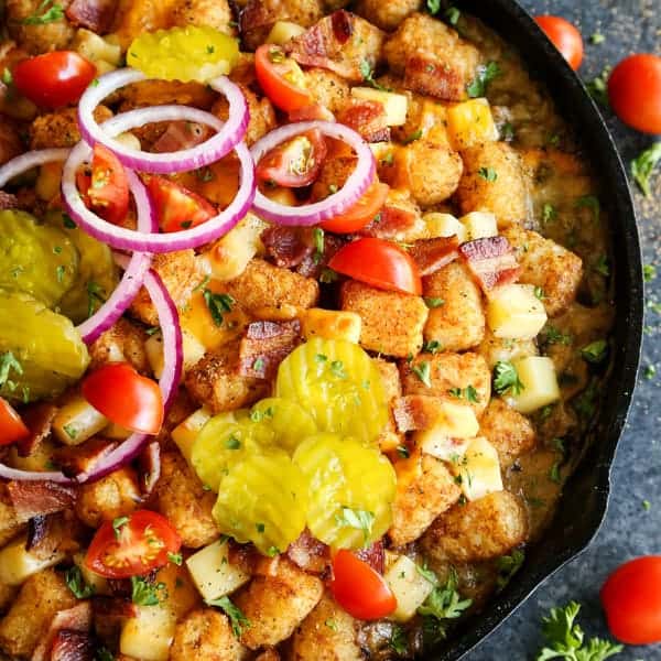 Tater tots with sliced pickles, tomatoes and red onion in a cast iron skillet