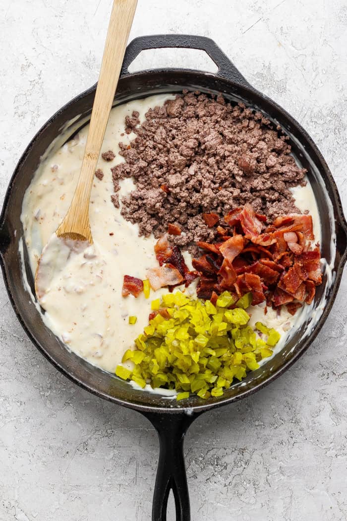 Beef, bacon, and pickles added to skillet of creamy sauce.