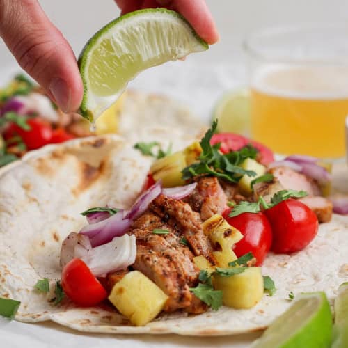 Squeezing lime juice onto grilled pork and pineapple taco