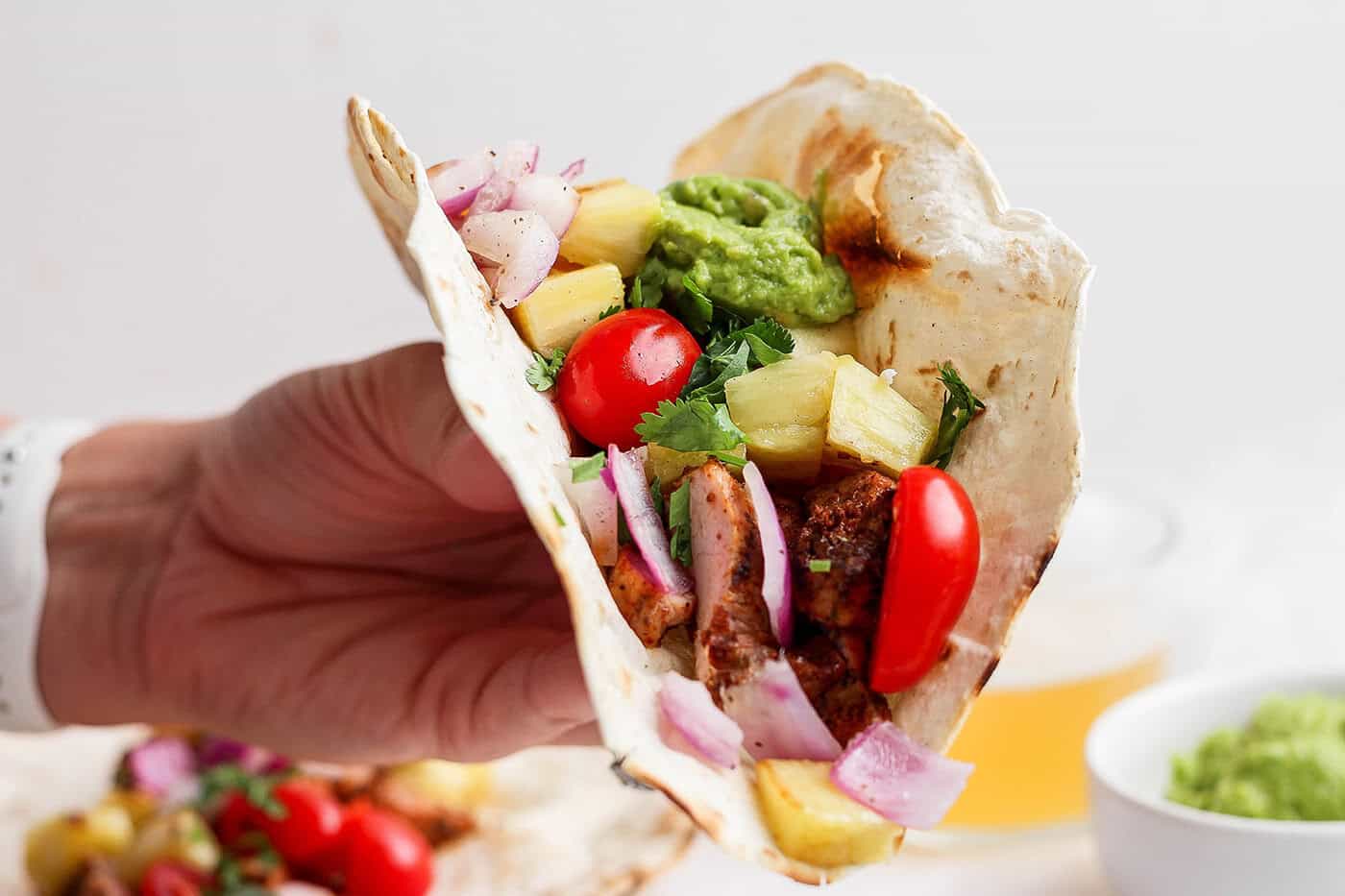 Hand holding grilled pork and pineapple taco