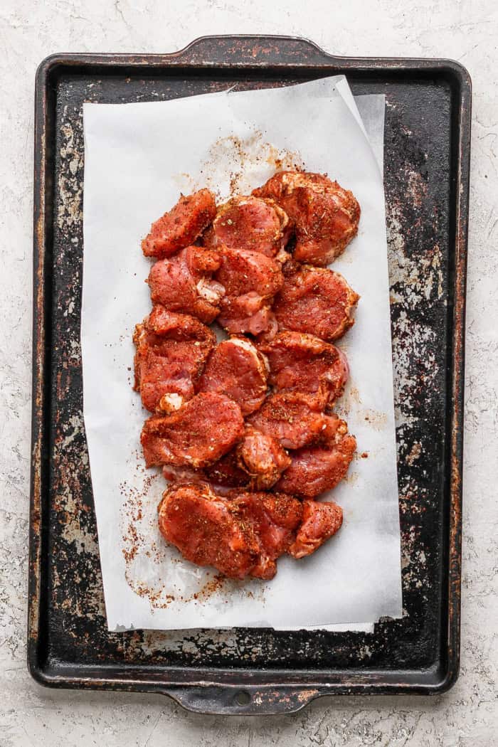 Overhead view of seasoned pork tenderloin rounds on sheet pan before cooking