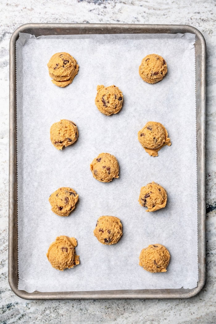 Balls of peanut butter chocolate chip cookie dough on sheet pan.