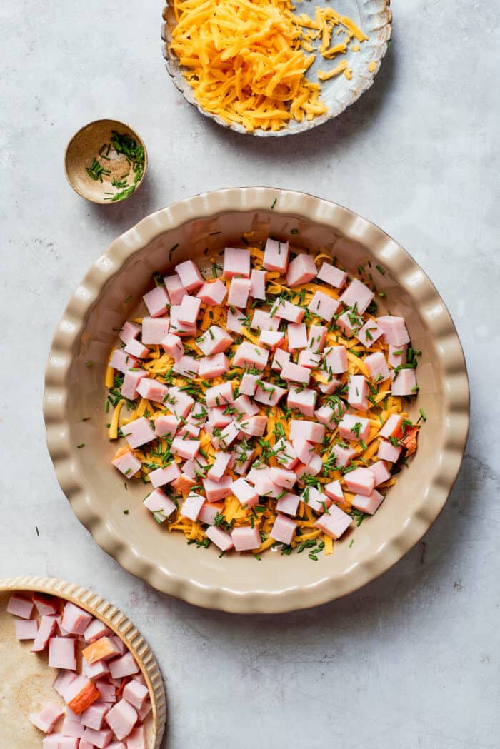 Assembling the layers of cheese, chives, and ham for the quiche. 