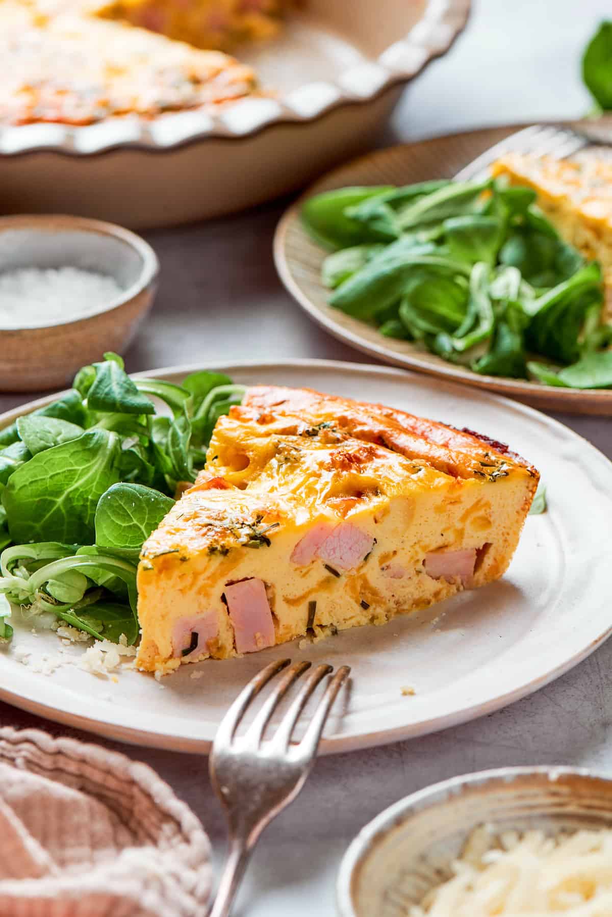 Close-up of a slice of creamy ham quiche on a serving plate with salad on the side.