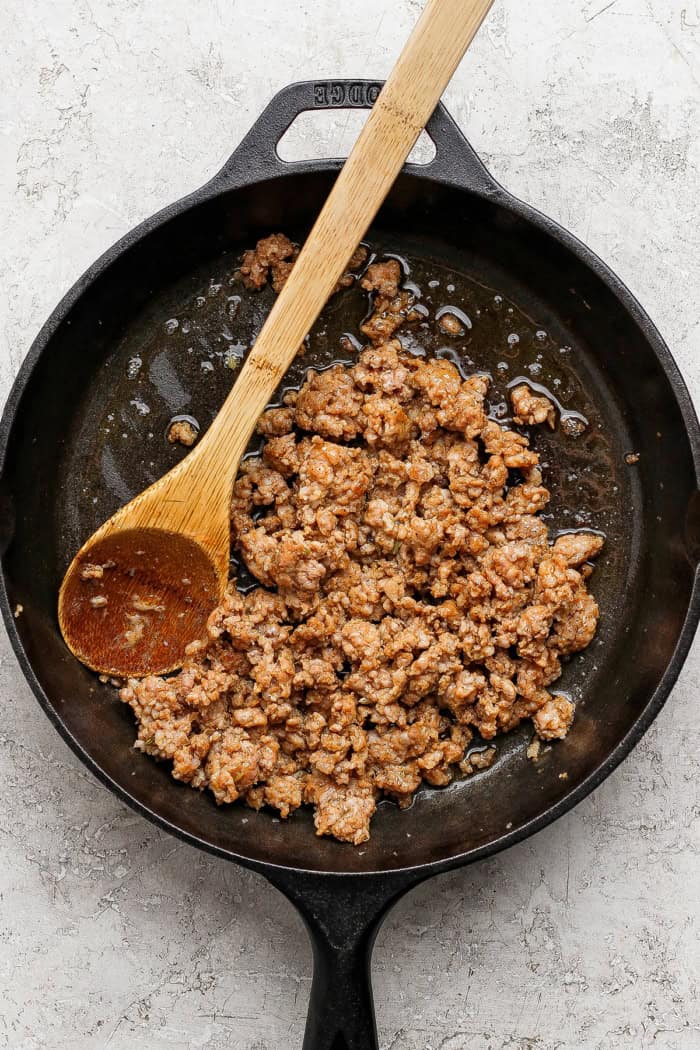 This skillet pizza with sausage has an Asian-inspired twist with chili garlic tomato sauce! A cast iron favorite with a crisp, chewy crust. Sausage browning in cast iron skillet.