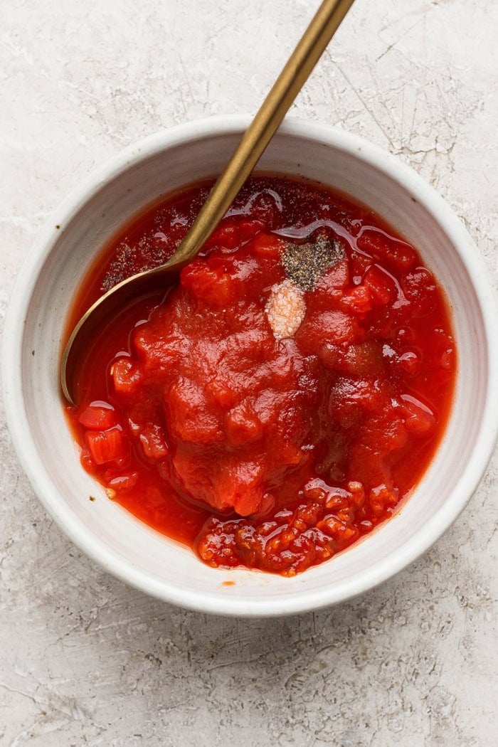Spoon in bowl of ingredients for chili garlic tomato sauce.