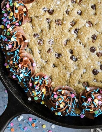 Chocolate chip skillet cookie in a cast-iron skillet with swirls of chocolate frosting and sprinkles around the outside