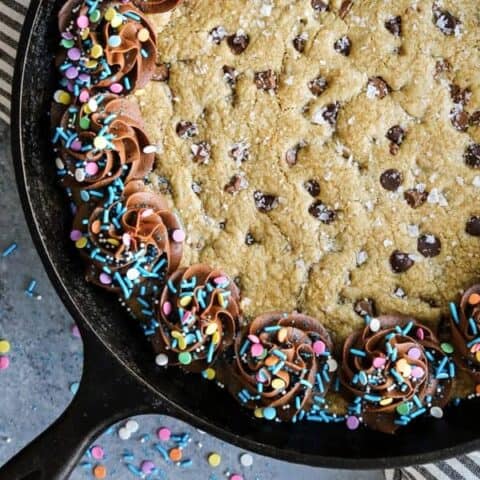 Chocolate chip skillet cookie in a cast-iron skillet with swirls of chocolate frosting and sprinkles around the outside