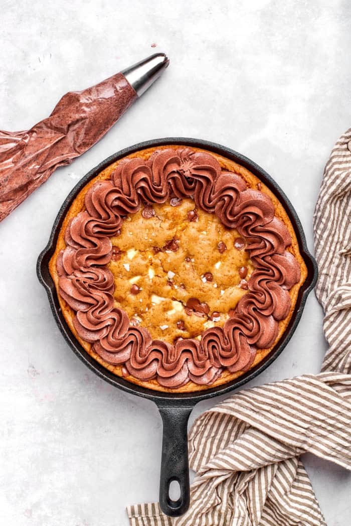 Chocolate buttercream piped onto chocolate chip cookie in cast iron skillet.