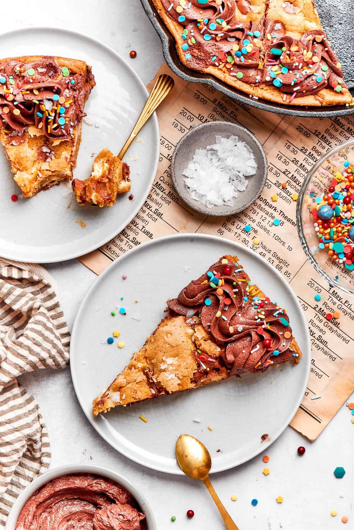 Two slices of chocolate chip skillet cookie on two plates with spoons.