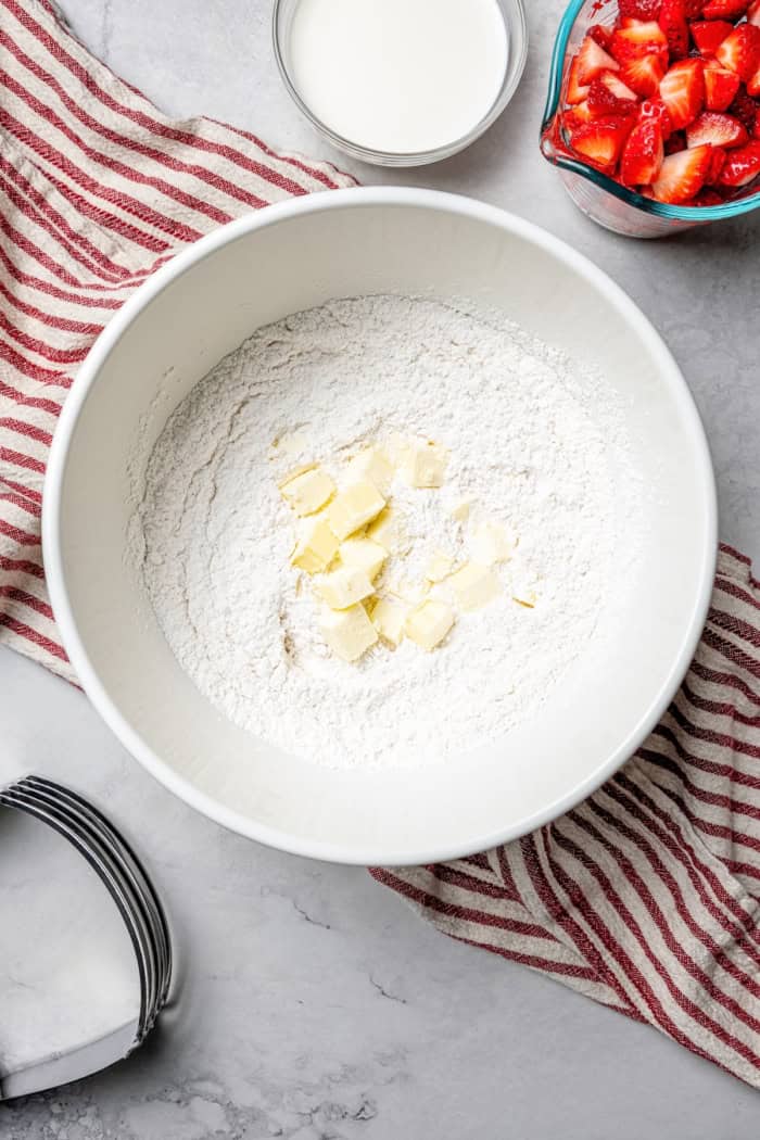 Overhead view of cubed butter added to bowl of dry ingredients for scones