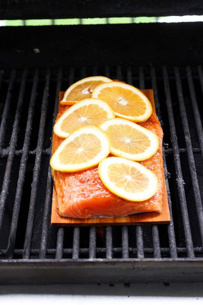 Grilled Chipotle-Orange Salmon is sweet, smoky and just a bit spicy, with irresistible caramelized edges. An easy recipe that feels special! Cedar plank on grill with raw salmon fillet and oranges