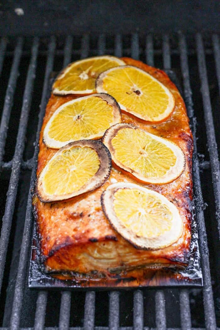 Grilled Chipotle-Orange Salmon is sweet, smoky and just a bit spicy, with irresistible caramelized edges. An easy recipe that feels special! Cedar plank on grill grates with salmon fillet and orange slices on top