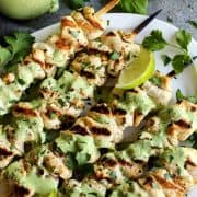 Overhead view of grilled chicken skewers on platter with sauce and lime wedges