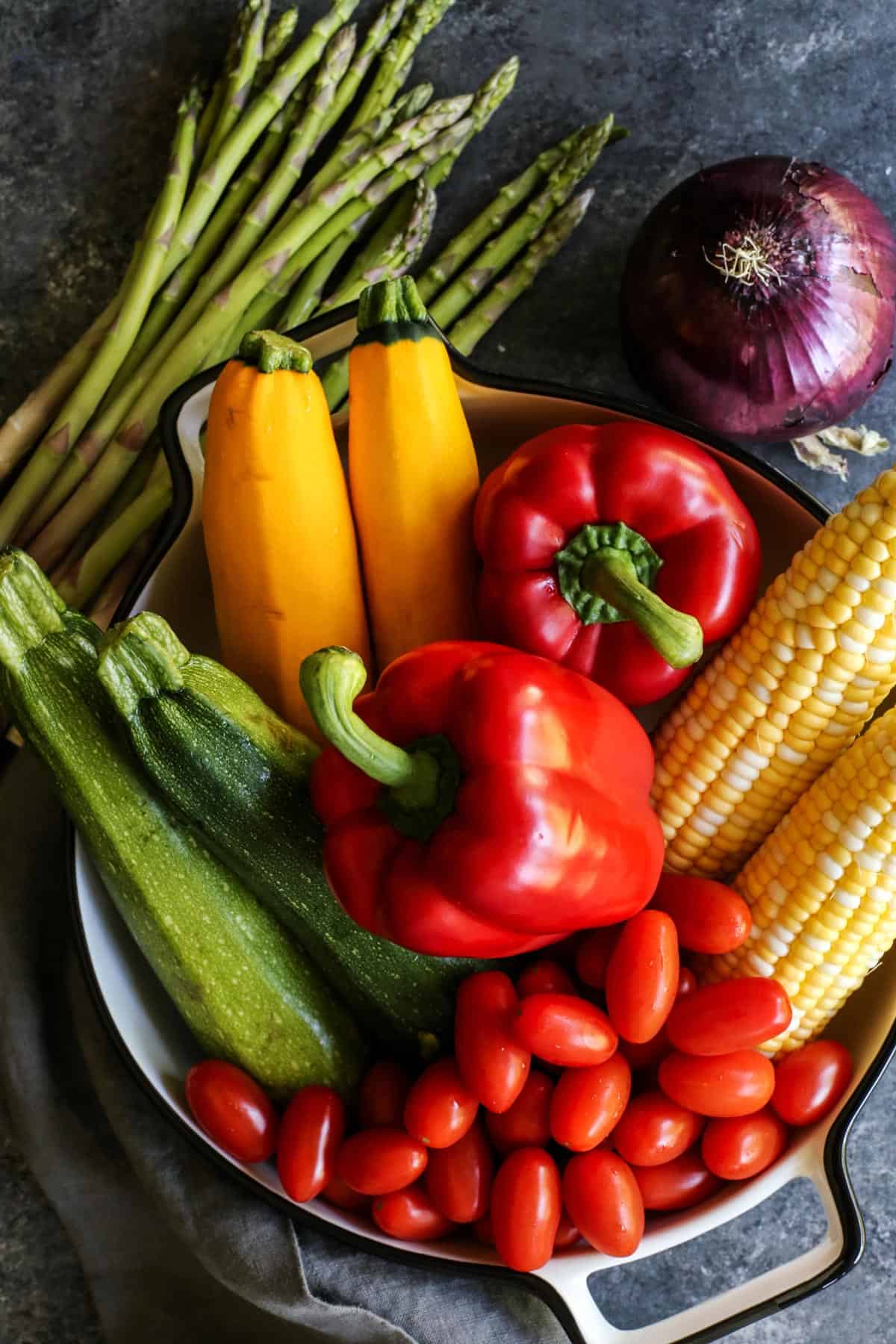 fresh whole vegetables: asparagus, zucchini, yellow squash, red peppers, red onion, sweet corn, tomatoes