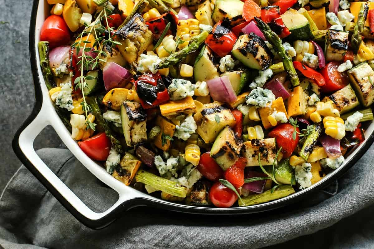 large white dish of grilled vegetable salad with blue cheese crumbles