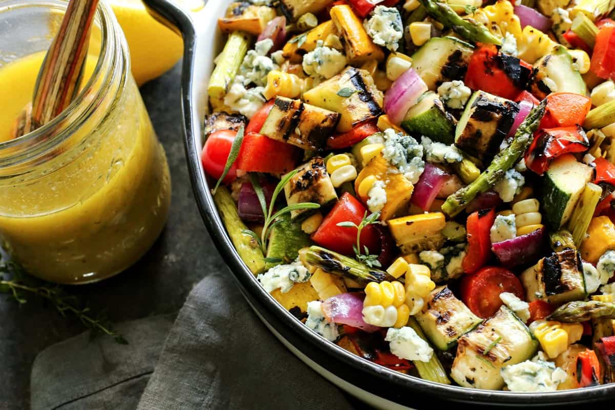 a salad of grilled, cut vegetables and a jar of herby lemon vinaigrette