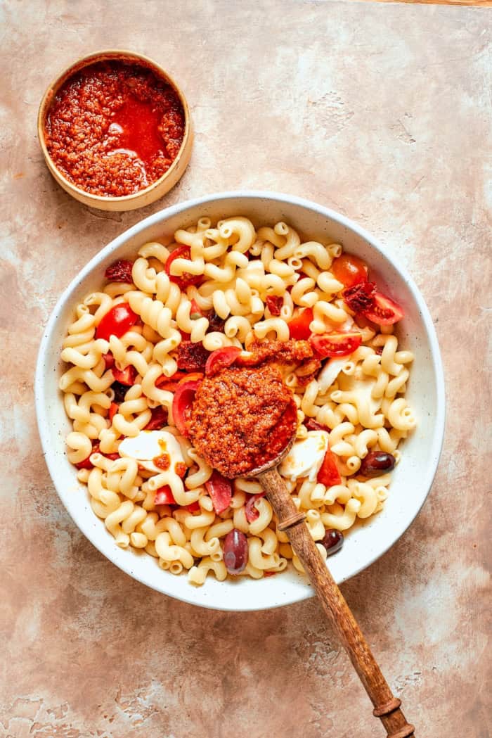 This sun-dried tomato pasta salad lets the abundance of summer produce shine, with juicy tomatoes and fresh basil. Perfect for picnics! Spoonful of dressing set in bowl of pasta salad.