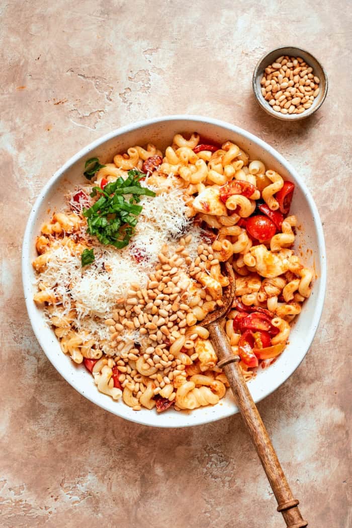 This sun-dried tomato pasta salad lets the abundance of summer produce shine, with juicy tomatoes and fresh basil. Perfect for picnics! Stirring Parmesan, basil, and pine nuts into sun-dried tomato pasta salad.