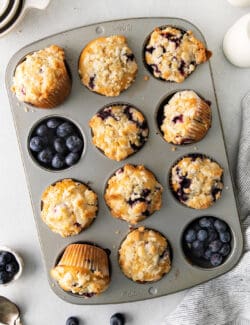 Overhead view of homemade blueberry muffins in a muffin tin with fresh blueberries filling the empty cups