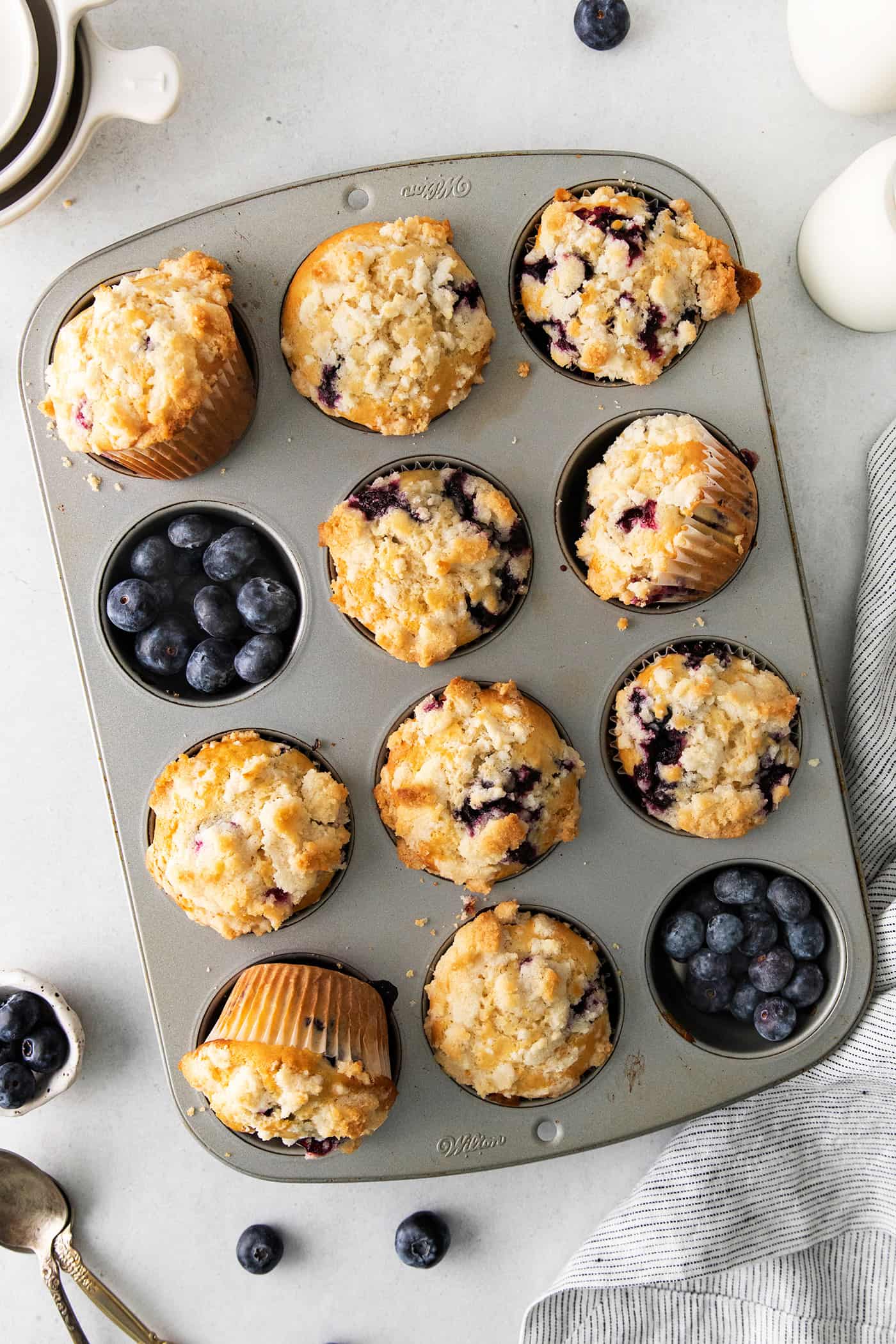 Overhead view of homemade blueberry muffins in a muffin tin with fresh blueberries filling the empty cups