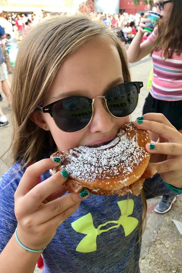 girl with sunglasses on, biting into a fluffernutter sandwich sprinkled with powdered sugar
