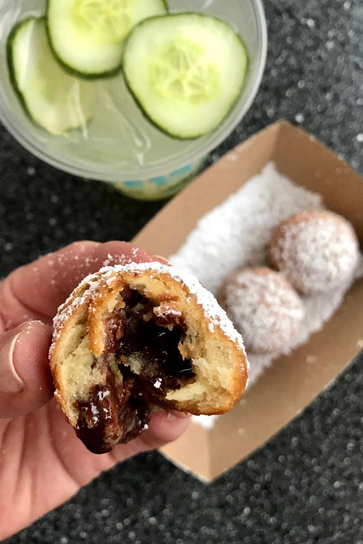 a bite out of a mini sconut, plus a drink with cucumber slices floating in it